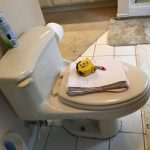 Toilet with a notebook, pen and tape measure stacked on top of lid