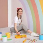 A woman paints a rainbow on the wall of a business